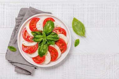 Canlı ve iştah açıcı bir Caprese antipasti. İçinde olgun domatesler, taze mozarella ve aromatik fesleğen yaprakları var.