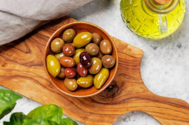 Bir kâse ve zeytin yağı şişesinde sunulan çeşitli zeytinlerin değişik renkleri, dokuları ve tatları sergilenmektedir.