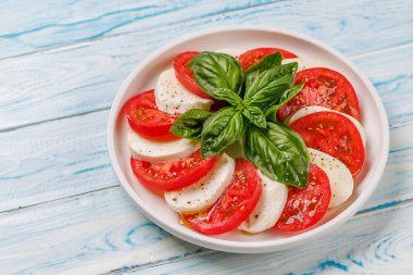 Canlı ve iştah açıcı bir Caprese antipasti. İçinde olgun domatesler, taze mozarella ve aromatik fesleğen yaprakları var.