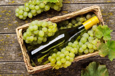 Taze üzümlerden oluşan bir yatağın üzerinde zarif bir şekilde duran bir şarap şişesi, yeşil ve mor üzümlerden oluşan zengin bir çeşitlilik sergiliyor.