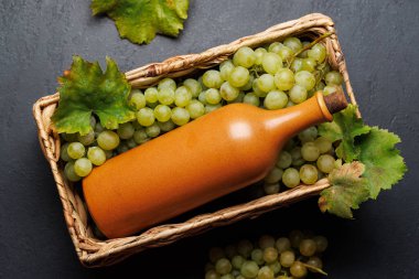 Taze üzümlerden oluşan bir yatağın üzerinde zarif bir şekilde duran bir şarap şişesi, yeşil ve mor üzümlerden oluşan zengin bir çeşitlilik sergiliyor.