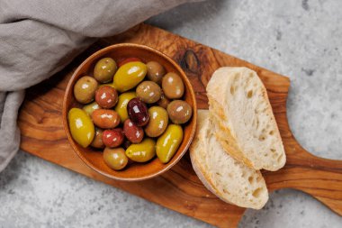 Bir kâse ve zeytin yağı şişesinde sunulan çeşitli zeytinlerin değişik renkleri, dokuları ve tatları sergilenmektedir.