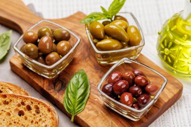 Bir kâse ve zeytin yağı şişesinde sunulan çeşitli zeytinlerin değişik renkleri, dokuları ve tatları sergilenmektedir.