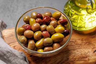 Bir kâse ve zeytin yağı şişesinde sunulan çeşitli zeytinlerin değişik renkleri, dokuları ve tatları sergilenmektedir.