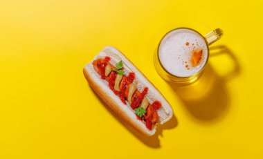 Canlı bir fotoğraf, bir bardak bira ve klasik sosisli, hepsi parlak sarı bir zemin karşısında, fotokopi alanı ile eğlenceli ve iştah açıcı bir sahne yaratıyor.