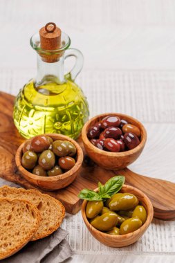 Bir kâse ve zeytinyağı şişesinde sunulan çeşitli zeytinler, farklı renkler, dokular ve tatlar sergileniyor. Kopyalama alanı ile