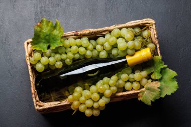 Taze üzümlerden oluşan bir yatağın üzerinde zarif bir şekilde duran bir şarap şişesi, yeşil ve mor üzümlerden oluşan zengin bir çeşitlilik sergiliyor.