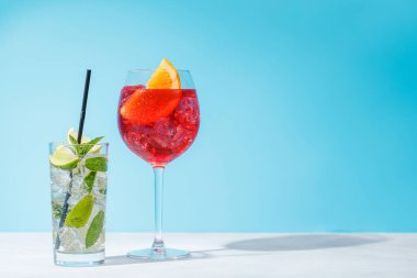 Masada açık mavi bir arkaplan üzerine çeşitli kokteyller serpiştirilmiş, güneşli parıltılar ve neşeli gölgelerle güçlendirilmiş.