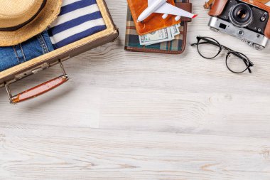 Elbiseli bir seyahat çantası, güneş şapkası, parmak arası terlik, ve ahşap arka planda düzenlenmiş bir kamera, düz konum tarzı, ürününüz için fotokopi alanı ile birlikte.