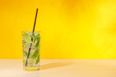 Masanın üzerine açık sarı bir arkaplan serpiştirilmiş mojito kokteyli, güneşli parıltılar ve neşeli gölgelerle güçlendirilmiş.