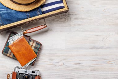 Elbiseli bir seyahat çantası, güneş şapkası, parmak arası terlik, ve ahşap arka planda düzenlenmiş bir kamera, düz konum tarzı, ürününüz için fotokopi alanı ile birlikte.