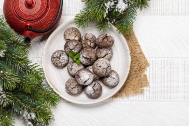 Çaydanlık ve köknar ağacının yanındaki tabağa yerleştirilmiş çeşitli Noel kurabiyeleri.