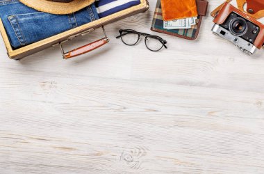 Elbiseli bir seyahat çantası, güneş şapkası, parmak arası terlik, ve ahşap arka planda düzenlenmiş bir kamera, düz konum tarzı, ürününüz için fotokopi alanı ile birlikte.