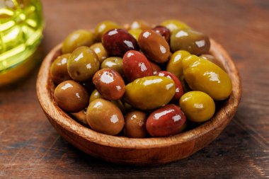 Bir kâse ve zeytin yağı şişesinde sunulan çeşitli zeytinlerin değişik renkleri, dokuları ve tatları sergilenmektedir.