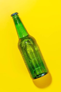 Parlak sarı bir arka plana karşı canlı soğuk bira şişesi. Görünür yoğunlaşma, keskin bir şekilde öne çık, canlı ve canlandırıcı bir görsel cazibe yarat