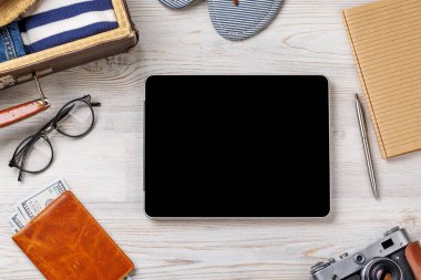 Boş ekran ve seyahat çantalı tablet, giysi, şapka, parmak arası terlik ve ahşap zemin üzerinde düzenlenmiş bir kamera, düz uzanma tarzı, metin ya da uygulama için kopyalama alanı ile