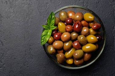 Bir kâse ve zeytin yağı şişesinde sunulan çeşitli zeytinlerin değişik renkleri, dokuları ve tatları sergilenmektedir.