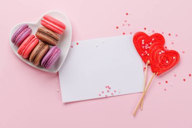 Various colorful macaroons in heart shaped bowl. Love sweets over pink background with greeting card clipart