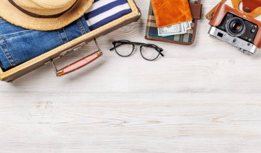 Elbiseli bir seyahat çantası, güneş şapkası, parmak arası terlik, ve ahşap arka planda düzenlenmiş bir kamera, düz konum tarzı, ürününüz için fotokopi alanı ile birlikte.