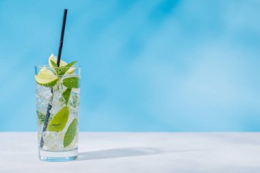 Masada açık mavi bir arkaplana karşı hazırlanmış bir mojito kokteyli, güneşli parıltılar ve neşeli gölgelerle geliştirilmiş.