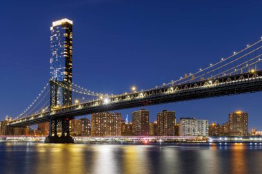 Manhattan Köprüsü 'nün panoramik günbatımı görüntüsü Manhattan' a doğru uzanıyor. Gökdelenler solgun gökyüzüne karşı sıcak renklerle aydınlanıyor.