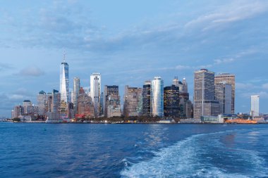 Manhattan şehir merkezinin canlı bir günbatımı manzarası nehirden izleniyor, gökdelenler sıcak, altın renklerle aydınlatılıyor.