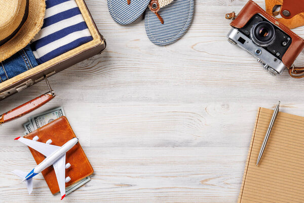 A travel bag with clothes, sun hat, flip flops, and a camera arranged on a wooden background, flat lay style, with copy space for your product