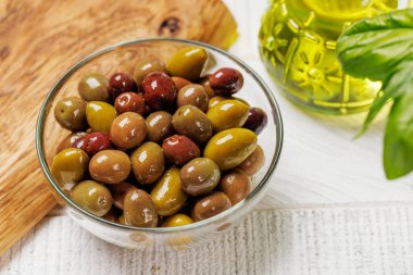 Bir kâse ve zeytin yağı şişesinde sunulan çeşitli zeytinlerin değişik renkleri, dokuları ve tatları sergilenmektedir.