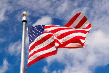Güneşli mavi gökyüzüne karşı dalgalanan Amerikan bayrağı, canlı renklerle vatansever gururunu sergiliyor.