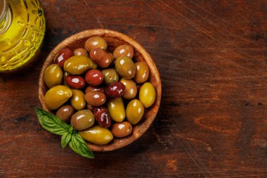 Bir kâse ve zeytin yağı şişesinde sunulan çeşitli zeytinlerin değişik renkleri, dokuları ve tatları sergilenmektedir.