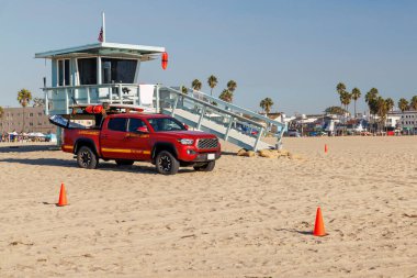 Classic lifeguard tower paired with a rescue vehicle parked nearby on a sandy beach under a clear blue sky. A timeless scene capturing the essence of beach safety and coastal life clipart