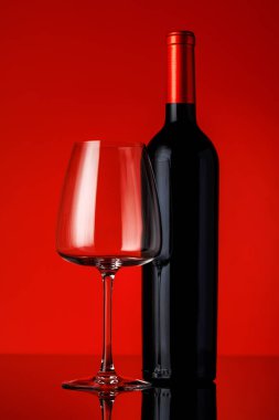 Kırmızı bir şarap şişesi, kırmızı bir zemine yerleştirilmiş bir kadeh şarap cesur ve zarif bir kompozisyon oluşturuyor.
