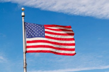 Güneşli mavi gökyüzüne karşı dalgalanan Amerikan bayrağı, canlı renklerle vatansever gururunu sergiliyor.