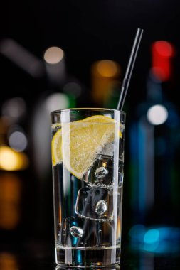 Bar masasında cin tonik kokteyli. Arka planda yanan şişelerin renkli bokeh 'i, dinamik ve canlı bir ortam yaratarak ortamı canlandırıyor.