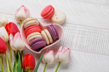 Pastel renkli laleler ve canlı kurabiyeler kalp şeklindeki bir kaseyi doldurur. Kutlamalar ve neşeli anlar için mükemmel ve büyüleyici bir sahne sunar.