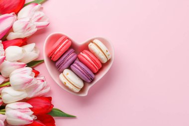 Pastel renkli laleler ve canlı kurabiyeler kalp şeklindeki bir kaseyi doldurur. Kutlamalar ve neşeli anlar için mükemmel ve büyüleyici bir sahne sunar.