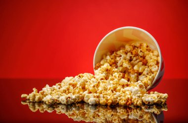 A box of fluffy popcorn against a vibrant red background, showcasing a classic striped design. The bright colors create an inviting, playful atmosphere perfect for a snack clipart