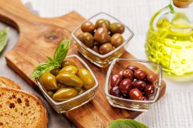 Bir kâse ve zeytin yağı şişesinde sunulan çeşitli zeytinlerin değişik renkleri, dokuları ve tatları sergilenmektedir.