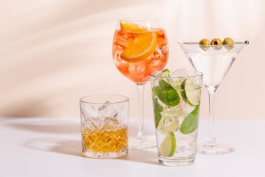 Parlak bir arka planda Aperol Spritz, Mojito ve Martini gibi canlı kokteyller sergilenmektedir. Karışımın ferahlatıcı ve renkli bir kutlaması