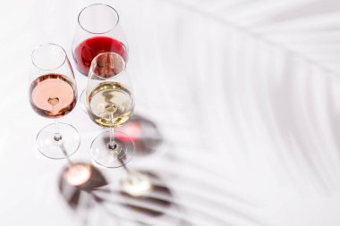 Kırmızı, beyaz ve gül şarabıyla dolu üç şarap kadehi parlak, minimalist arka planda zarif bir şekilde duruyor. Şarabın çeşitliliğinin ve zarafetinin canlı bir gösterisi.