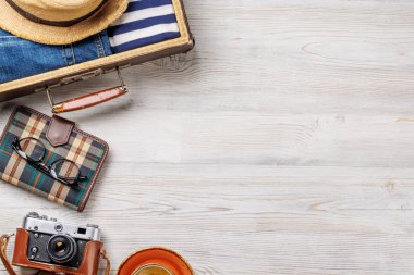 Elbiseli bir seyahat çantası, güneş şapkası, parmak arası terlik, ve ahşap arka planda düzenlenmiş bir kamera, düz konum tarzı, ürününüz için fotokopi alanı ile birlikte.