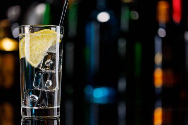 Bar masasında cin tonik kokteyli. Arka planda yanan şişelerin renkli bokeh 'i, dinamik ve canlı bir ortam yaratarak ortamı canlandırıyor.
