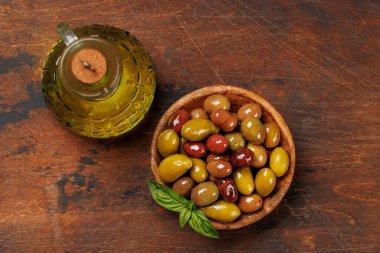 Bir kâse ve zeytin yağı şişesinde sunulan çeşitli zeytinlerin değişik renkleri, dokuları ve tatları sergilenmektedir.