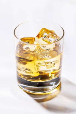 Buzların üzerinde rafine edilmiş bir bardak viski. Kehribar rengi, buz küpleri yavaşça erirken parlıyor. Temiz ve zarif bir sunum için parlak beyaz bir arkaplana kuruluyor.