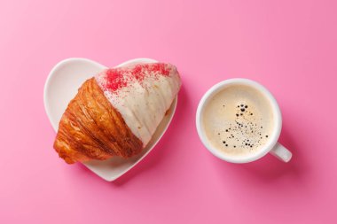 Nefis bir kahve ve ahudududulu kruvasan eşleşmesi, yumuşak pembe bir arka plan üzerine kurulmuş, rahat ve hoşgörülü bir an için mükemmel.