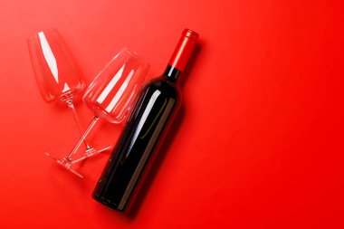 Zarif kırmızı şarap kadehleri ve kırmızı arka planda eşleşen kırmızı şarap şişesi lüks ve sofistike bir sahne yaratıyor.