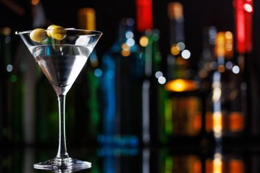 Bar masasında martini kokteyli. Arka planda yanan şişelerin renkli bokeh 'i, dinamik ve canlı bir ortam yaratarak ortamı canlandırıyor.