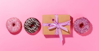 Renkli malzemelerle dolu canlı çörekler ve pembe bir arka planda hediye kutusu olan bir apartman dairesi. Sevgililer Günü kutlamaları için mükemmel.