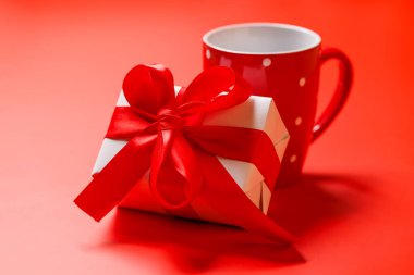 Güzel paketlenmiş bir hediye kutusunun yanında sıcak bir kahve fincanı. İkisi de canlı kırmızı bir arka plana yerleştirilmiş. Kutlamalar için mükemmel bir sahne ya da düşünceli bir hediye.