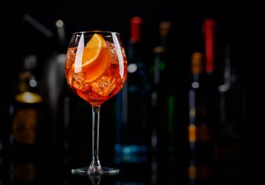 Bar masasında Aperol sprey kokteyli. Arka planda yanan şişelerin renkli bokeh 'i, dinamik ve canlı bir ortam yaratarak ortamı canlandırıyor.